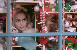 Emilia Clarke looks through a window of the Christmas shop in LAST CHRISTMAS (2019).